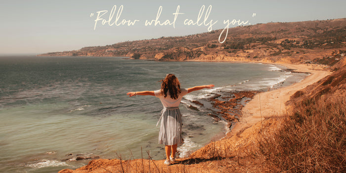 Back view of a girl with arms open, looking at the ocean. “Follow what calls you.” is written above.